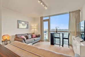 A modern hotel room with a sofa, a dining table with chairs, a TV, and a large window with a view. - Delightful Apartment Wandsworth (London)