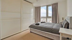 Ein Schlafzimmer mit Bett, einem Vorhangfenster, einem Nachttisch und Blick auf die Stadt.