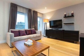 Ein modernes Wohnzimmer mit einer Couch, einem Couchtisch, einem Fernseher und einer Lampe.