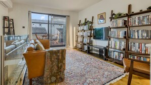 A spacious living room with a large window, a bookshelf, and a sofa. - Zen Chelsea Townhouse 3BR 3 5BA Terrace (London)