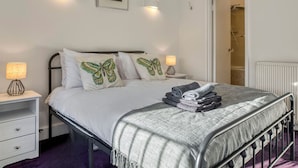 A bedroom with a bed, two bedside tables, a wall-mounted light, a framed picture, and a door leading to a bathroom. - Zen Chelsea Townhouse 3BR 3 5BA Terrace (London)