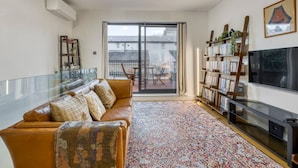 A living room with a sofa, a glass table, a bookshelf, a TV, and a balcony with a view. - Zen Chelsea Townhouse 3BR 3 5BA Terrace (London)