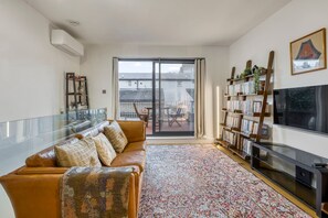 A living room with a sofa, a glass table, a bookshelf, a TV, and a balcony with a view. - Zen Chelsea Townhouse 3BR 3 5BA Terrace (London)