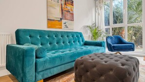 Un sofá color turquesa, un otoman oscuro y una silla azul en una habitación con un ventanal grande y un cuadro en la pared.
