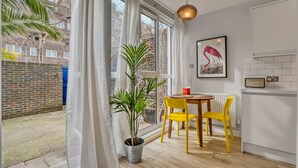 Una habitación con una mesa de comedor, sillas, una planta en maceta, un radiador y una ventana con cortinas.