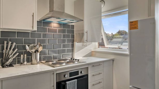 Una cocina moderna con armarios grises, un salpicadero de azulejos negros, electrodomésticos de acero inoxidable y una ventana con vistas.