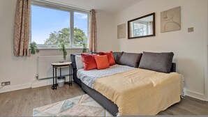 Un dormitorio con cama, ventana, radiador, planta y obras de arte en la pared.
