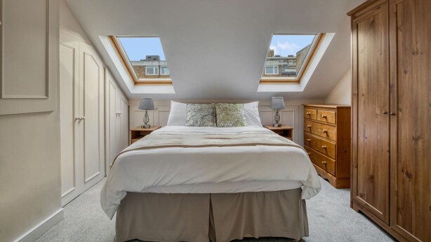 A bedroom with a skylight, a bed, a dresser, and a wardrobe. - Spacious 4BR 3BA House Near Barons Court Station (London)