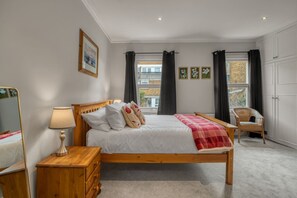 Ein Schlafzimmer mit einem hölzernen Bett, einem Nachttisch, einer Lampe, einem Stuhl und einem Fenster mit Vorhängen.