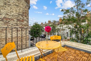Ein Balkon mit Backsteinmauer, schmiedeeisernem Geländer, einem gelben Tisch mit einer Vase und einem gelben Stuhl.