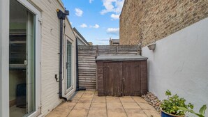 A narrow courtyard with a tiled floor, a wooden fence, and a potted plant. - Spacious 4BR 3BA House Near Barons Court Station (London)