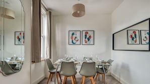 A modern dining room with a glass table, grey chairs, and abstract wall art. - Chic 1bed w Patio Battersea (London)