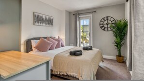 A bedroom with a bed, a bedside table, a wall clock, a window, and a potted plant. - Chic 1bed w Patio Battersea (London)