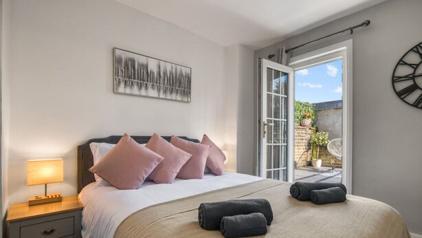 A bedroom with a bed, bedside table, and a view through a glass door. - Chic 1bed w Patio Battersea (London)