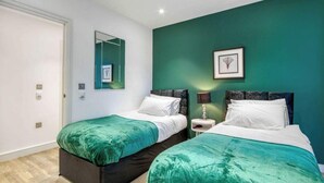 A twin bedroom with two beds, a mirror, a framed picture, and a nightstand with a lamp. - Modern 2 Bedroom Flat (London)