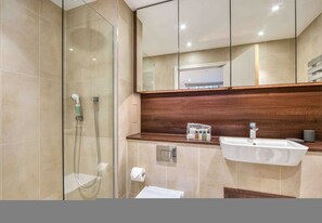 A modern bathroom with a glass shower enclosure, a wooden vanity, and a large mirror. - Modern 2 Bedroom Flat (London)