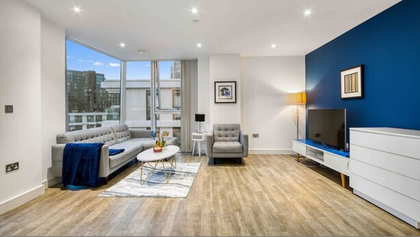 A modern living room with a sofa, armchair, coffee table, and TV stand. - Modern 2 Bedroom Flat (London)