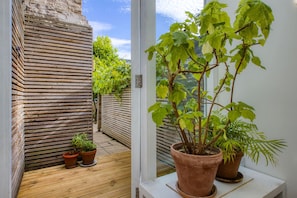 Une terrasse en bois, une plante en pot et une fenêtre donnant sur un jardin.