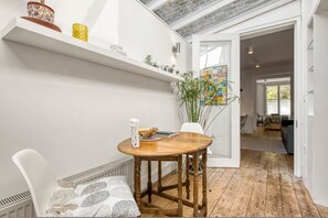 Un coin repas avec une table en bois, des chaises blanches et une étagère blanche ornée d’objets décoratifs.