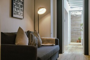 Un salon moderne avec un canapé, des coussins, une lampe sur pied et un tableau encadré au mur.