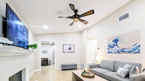 Un salon moderne avec une cheminée, un canapé gris, une table basse, un ventilateur de plafond et un grand téléviseur.