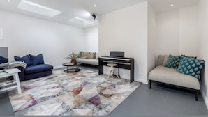 En moderne stue med sofa, sofabord, klaver og et mønstret gulvtæppe.