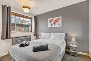 A hotel room with a bed, a window with curtains, a world map artwork, a bedside lamp, and a small table. - 107 Stonhouse Street Lovely 3-bed Clapham Common (London)