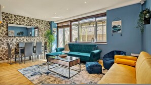 A living room with a sofa, coffee table, and chairs, a dining area with a table and chairs, and large windows with a view. - 107 Stonhouse Street Lovely 3-bed Clapham Common (London)