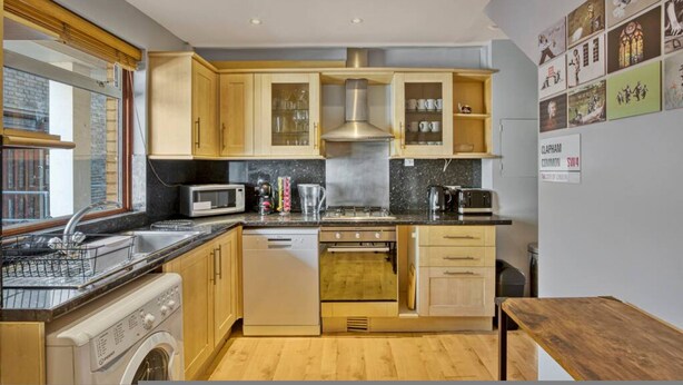 A compact kitchen with wooden cabinets, a microwave, a stove, and a dishwasher. - 107 Stonhouse Street Lovely 3-bed Clapham Common (London)