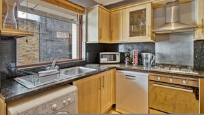 A compact kitchen with a microwave, stove, sink, and wooden cabinets. - 107 Stonhouse Street Lovely 3-bed Clapham Common (London)