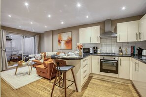 A modern kitchen with a central island, white cabinetry, and a dining area with a sofa and chairs. - Notting Hill Hyde Park - Cosy 2 Bed 2 Bath (London)