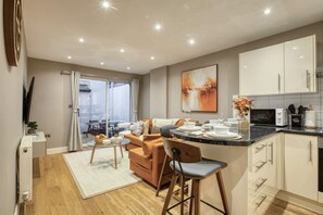A modern kitchen with white cabinets, a dining area with a sofa and table, and a large window. - Notting Hill Hyde Park - Cosy 2 Bed 2 Bath (London)