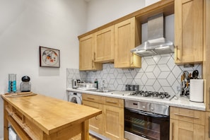 A modern kitchen with wooden cabinets, a stainless steel stove, and a tiled backsplash. - Vibrant 2-bed by Bow (London)