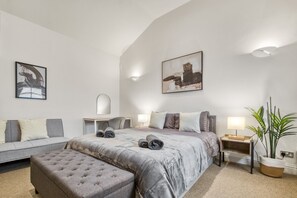 Een slaapkamer met een bed, een slaapbank, een nachtkastje, een lamp, een potplant en kunst aan de wanden.