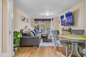A living room with a sofa, coffee table, and dining table, a TV mounted on the wall, and a window with a view. - Tranquil Apartment Southwark (London)