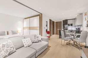 Ein modernes Wohnzimmer mit einer Couch, einem Esstisch und Stühlen, einer Küchenzeile mit Geräten sowie einem Flur, der zu einer Tür führt.
