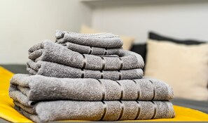 A neatly folded stack of towels on a bed with a yellow blanket. - Quirky Studio in Central Reading (Reading)
