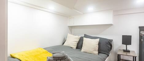 Ein Schlafzimmer mit einem Bett, einem Nachttisch mit Lampe, einer gelben Decke und einem Stapel Handtücher.