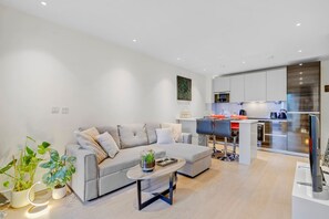 Uma sala de estar moderna com um sofá cinza, uma mesa de centro e plantas em vasos.