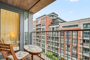 Uma varanda com mesa e cadeiras, uma porta de vidro e vista para edifícios altos.