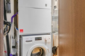 A compact laundry area with a Bosch washing machine and dryer, a purple hose, and a door with a key lock. - Cosy Manhattan Studio w Balcony (London)