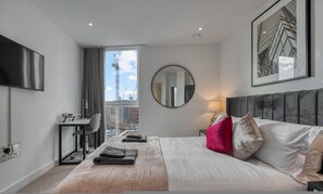 Ein modernes Hotelzimmer mit Bett, Schreibtisch, Stuhl, rundem Spiegel und Fenster mit Blick auf die Stadt.
