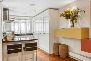 Una cocina moderna con una isla central, taburetes de bar y un florero sobre una estantería.