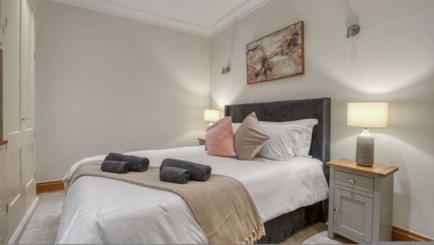 Una camera da letto ordinata con un letto, abat-jour, un quadro e un comodino.