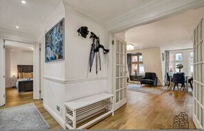 A spacious room with a wooden floor, a white bench, a painting, and a door leading to another room. - Spectacular 2 Bed Mayfair (London)