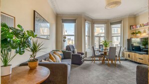 A living room with a sofa, a dining table, chairs, a TV, and potted plants. - 3bed Battersea Rise Books Charm and Style (London)