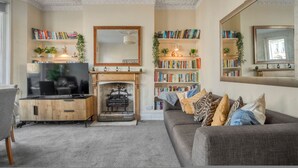A living room with a fireplace, bookshelves, a television, and a sofa. - 3bed Battersea Rise Books Charm and Style (London)