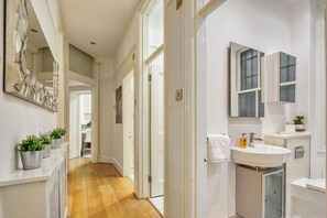 A hallway leading to a bathroom with a sink, mirror, and potted plants. - 2bed 2bath Apartment Earls Court (London)