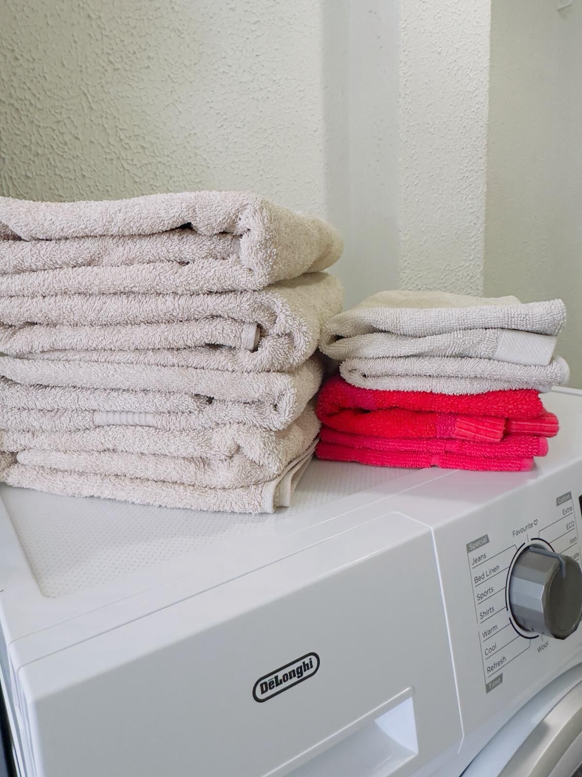 A Delonghi washing machine with a stack of folded towels on top.