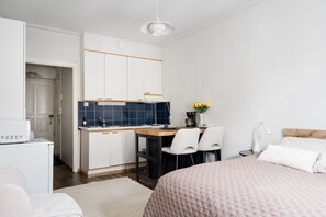 A compact bedroom with a bed, bedside table, and a small kitchenette area. - Premium Studio Apartment in the City (Helsinki)